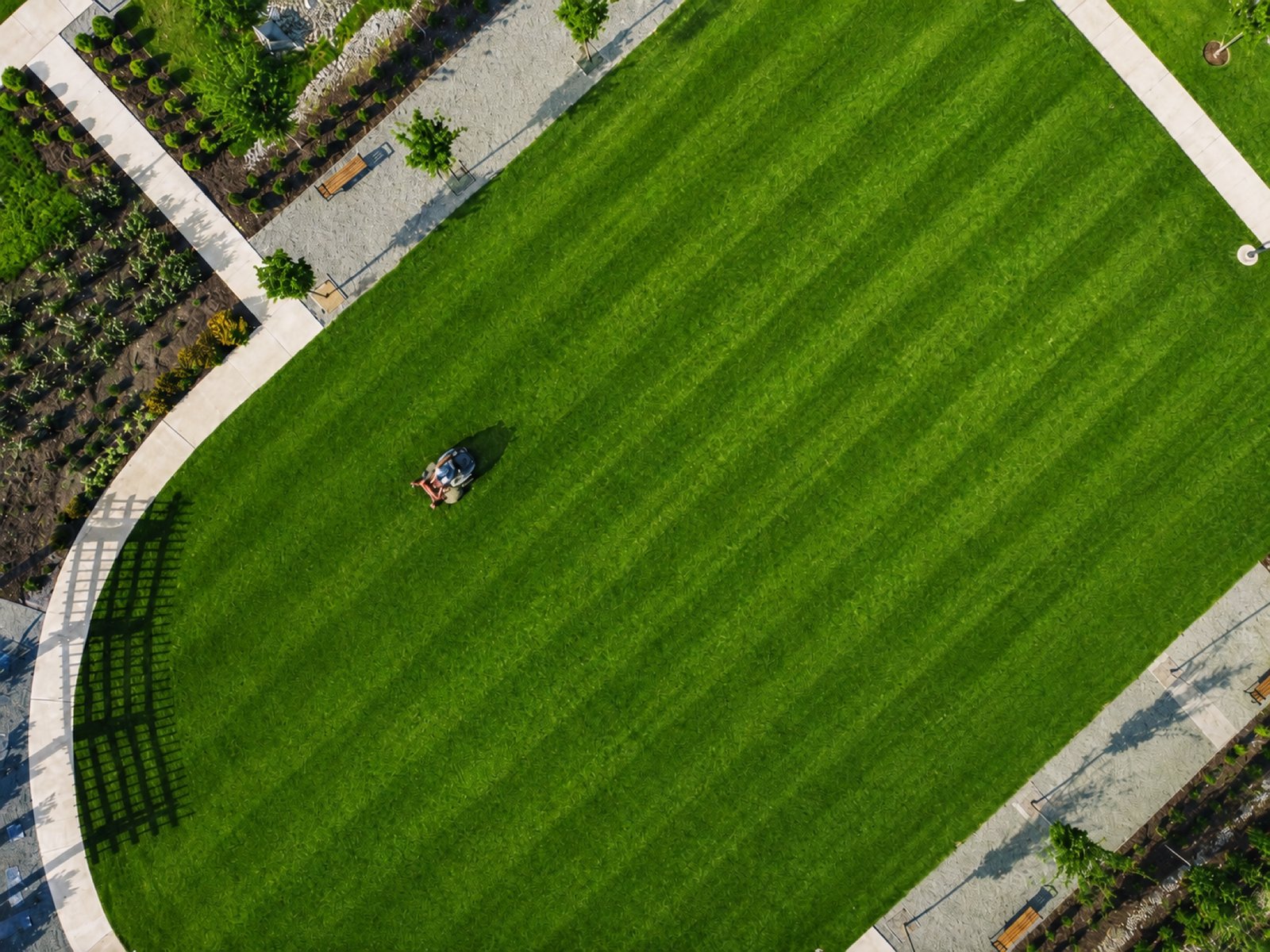Top-down aerial view of a mower cutting clean stripes into a large green lawn